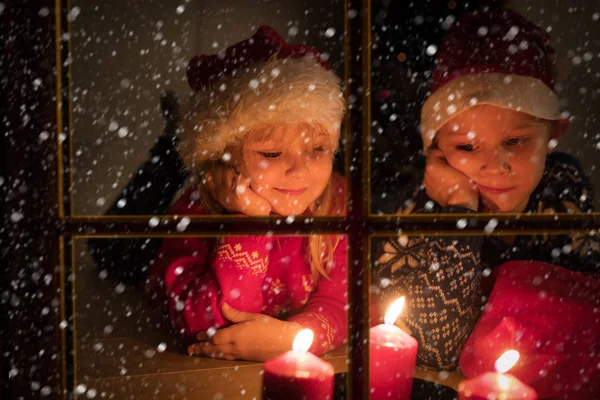 Μικρό αγόρι και κορίτσι κοιτάζοντας κεριά Χριστουγέννων που προβάλλονται από το εξωτερικό παράθυρο — Φωτογραφία Αρχείου