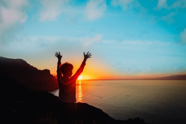 Mutlu çocuk siluetleri, deniz kıyısındaki günbatımı dağlarında seyahat etmekten zevk alır.