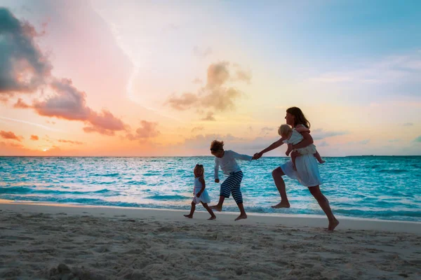 Mutter mit Kindern rennt und spielt am Strand bei Sonnenuntergang — Stockfoto