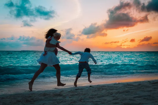 Mãe com crianças correr e jogar na praia ao pôr do sol — Fotografia de Stock