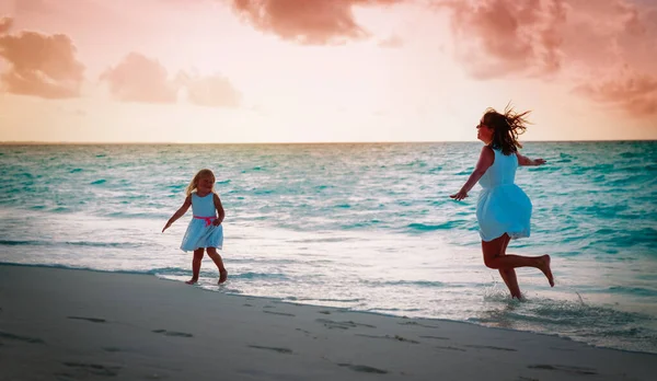 Mutter mit kleiner Tochter spielt bei Sonnenuntergang am Strand — Stockfoto