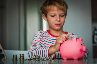 Çocuk para sayıyor, çocuk kumbaraya bozuk para koyuyor.