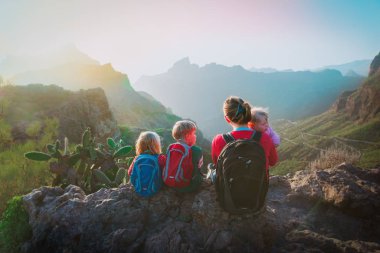 Anne ve üç çocuğu dağlarda yürüyüş yapıyor, aile doğada seyahat ediyor.