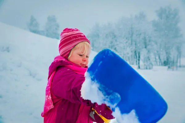 Χαριτωμένο κοριτσάκι σκάβουν χιόνι με φτυάρι, τα παιδιά παίζουν το χειμώνα — Φωτογραφία Αρχείου