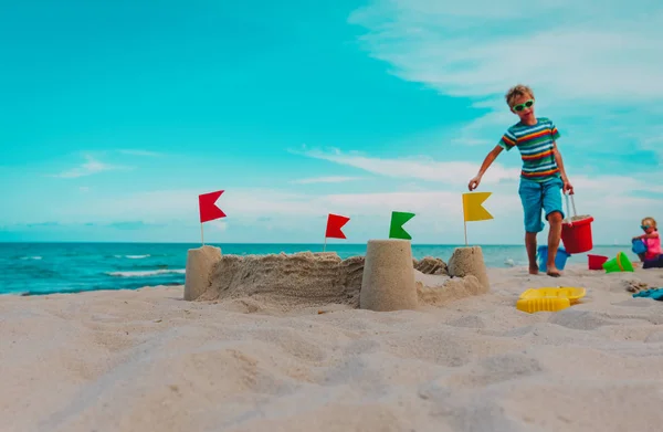 Castelo de areia e crianças construindo-o em férias na praia — Fotografia de Stock