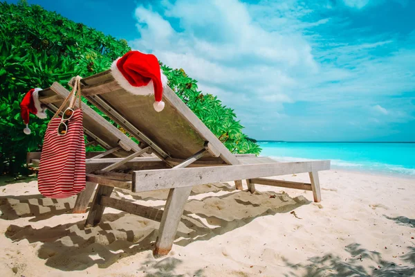 Natal em salões de cadeira de praia com chapéus de Santa no mar — Fotografia de Stock