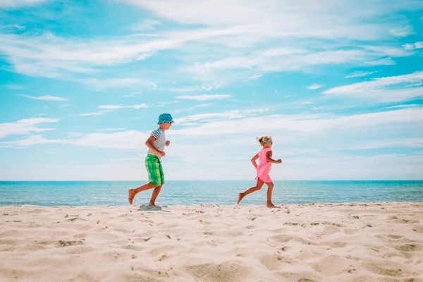 Щасливий милий хлопчик і дівчина біжить на пляжі, діти насолоджуються відпочинком на морі — стокове фото