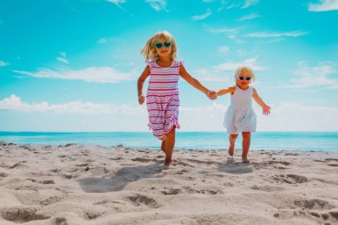 Güzel küçük kızlar sahilde koşar, çocuklar deniz tatilinin tadını çıkarır.