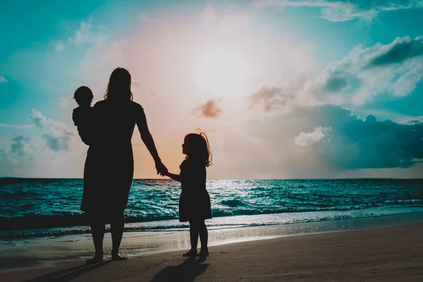 Mãe com dois filhos andando na praia ao pôr do sol — Fotografia de Stock