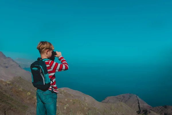 Junge schaut durch Fernglas auf Reisen in den Bergen am Meer — Stockfoto