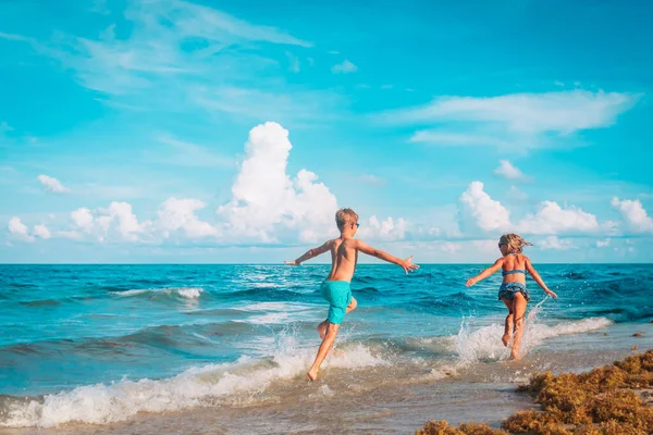 Gelukkig meisje en jongen run, kinderen vliegen en spelen met golven op het strand — Stockfoto