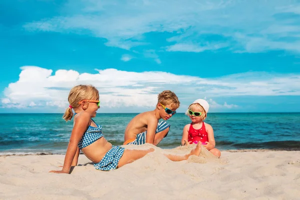 Miúdos, rapazes e raparigas, brincam com areia na praia. — Fotografia de Stock
