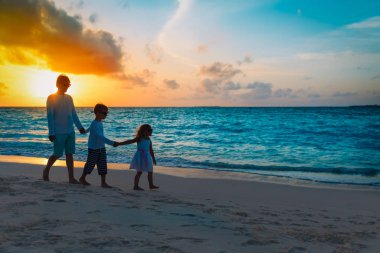 Baba ve çocuklar gün batımında sahilde yürüyorlar.