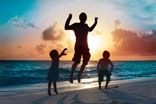Отец с двумя детьми играет на пляже на закате — стоковое фото