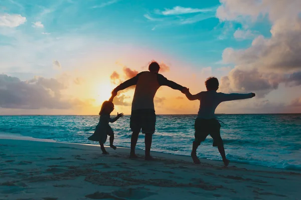 Vader met twee kinderen spelen op het strand bij zonsondergang — Stockfoto
