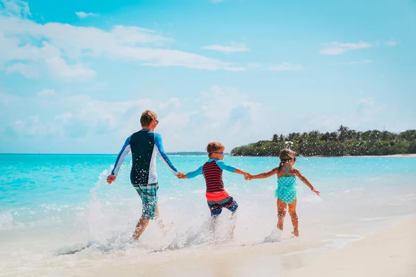 Vader met kinderen spelen met water, familie gerund op het strand — Stockfoto