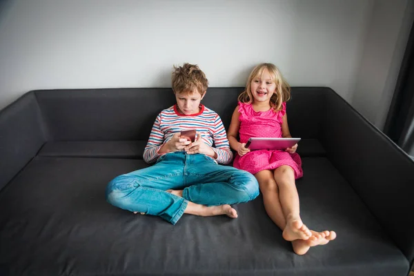 Niño y niña con teléfono móvil y almohadilla táctil en casa —  Fotos de Stock
