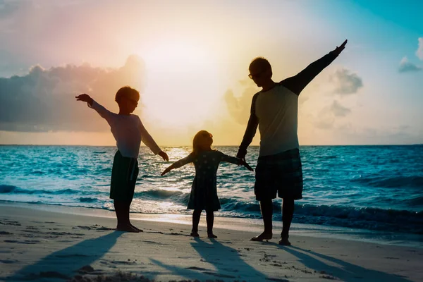 Padre con hijo e hija siluetas jugar al atardecer playa — Foto de Stock