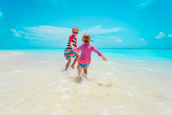 Klein meisje en jongen lopen spelen met water op het strand — Stockfoto