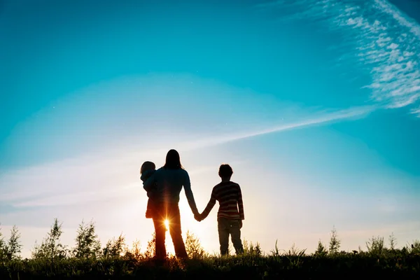 Lycklig mor med son och dotter som håller hand i solnedgången natur — Stockfoto