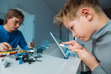 Erkek çocuk robot yapıyor ve sınıfta öğretmenle birlikte dokunmatik ped ile programlıyor.