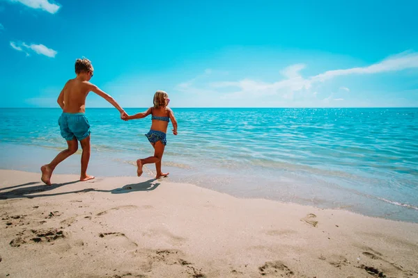 Gelukkige jongen en meisje rennen om te zwemmen op het strand — Stockfoto