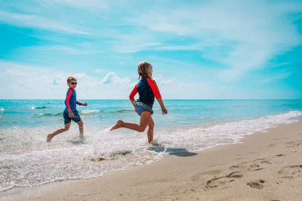 Šťastný dívka a chlapec běh a hrát si s vodou na pláži — Stock fotografie