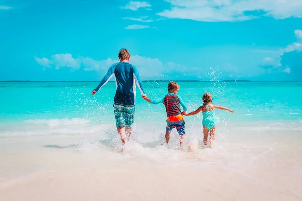 Otec s dětmi si hraje s vodou, rodinný běh na pláži — Stock fotografie