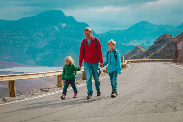 Father with two kids walking on road in mountains — Stockfoto