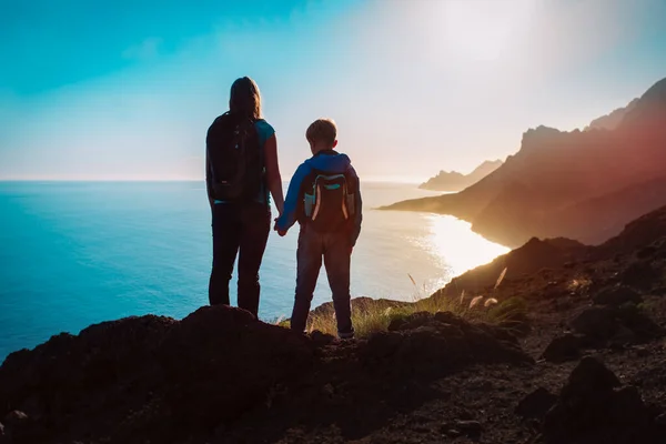 Silhueta de mãe e filho viajar em montanhas pôr do sol perto do mar — Fotografia de Stock