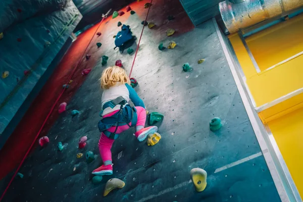 Mała dziewczynka wspina się na sztuczne głazy ściany w siłowni — Zdjęcie stockowe