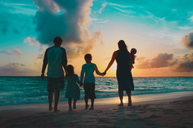 Çocuklu mutlu bir aile gün batımında sahilde yürüyor.
