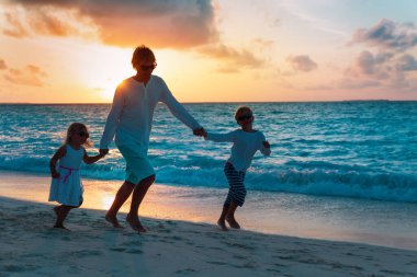 father and two kids play on beach at sunset