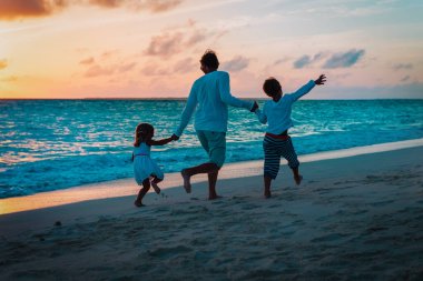 father and two kids play on beach at sunset