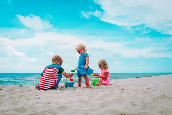 Miúdos, rapazes e raparigas, brincam com areia na praia. — Fotografia de Stock