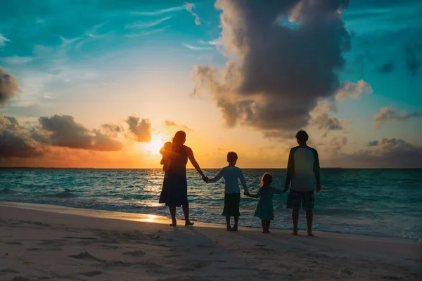 Çocuklu mutlu bir aile gün batımında sahilde yürüyor. — Stok fotoğraf