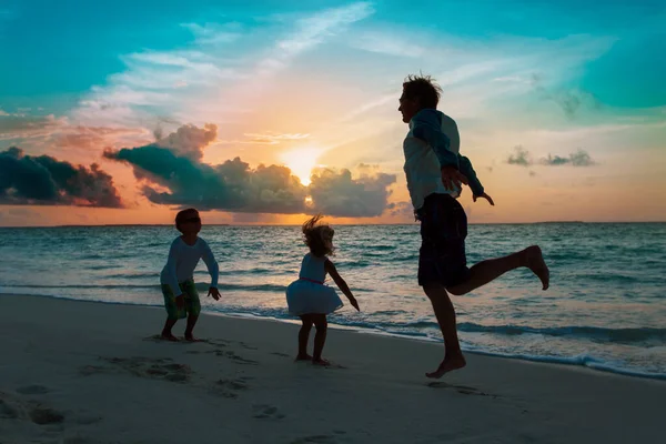 Mutlu bir baba ve çocuklar günbatımı kumsalında neşe içinde atlıyorlar. — Stok fotoğraf