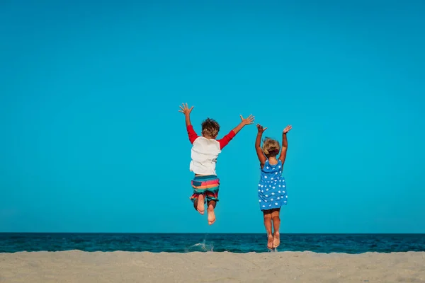 Gelukkig weinig jongen en meisje geniet van speel sprong op strand — Stockfoto