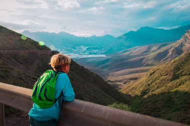 Çocuk dağlarda gezer, çocuklar manzaraya bakar.