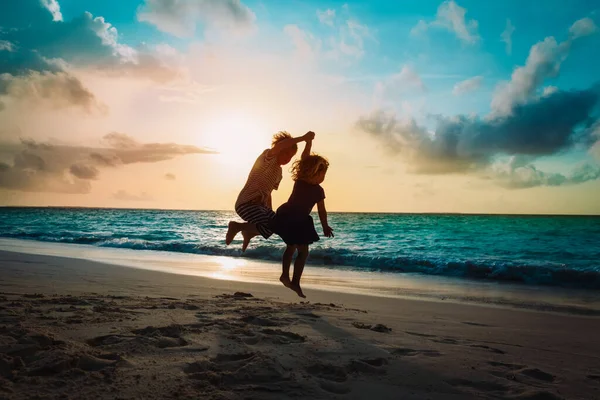 Kinder haben Spaß, Jungen und Mädchen springen am Strand bei Sonnenuntergang — Stockfoto