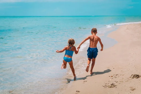 Mutlu kız ve erkek koşar sahilde dalgalarla oynarlar — Stok fotoğraf