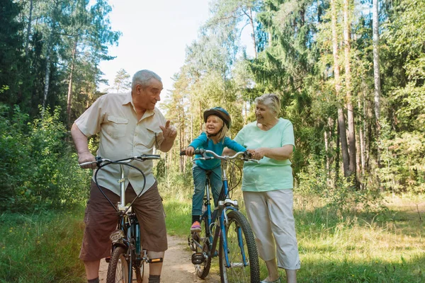 Активная пожилая пара с маленькой внучкой на велосипедах на природе — стоковое фото
