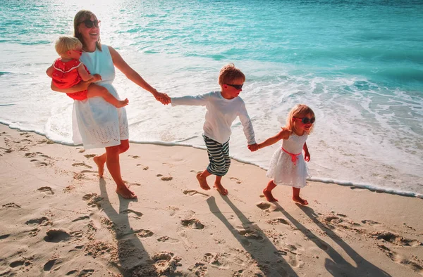 Moeder met kinderen spelen run op strand bij zonsondergang — Stockfoto