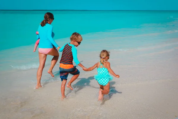 Moeder met kinderen spelen met water lopen op strand — Stockfoto