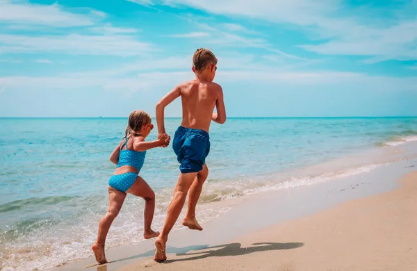 Dívka a chlapec běh a hrát si s vodou na pláži — Stock fotografie