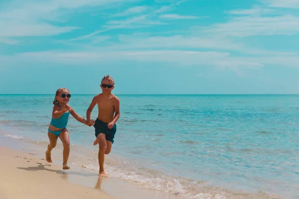 Счастливые девочка и мальчик бегают и играют с водой на пляже — стоковое фото