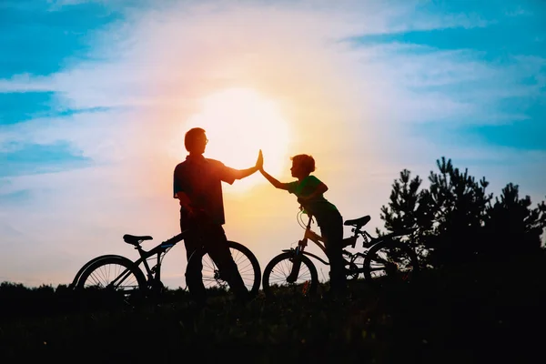 Silhueta de feliz pai e filho de bicicleta ao pôr do sol — Fotografia de Stock