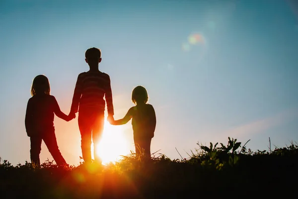Silhuetas de crianças - menino e meninas - de mãos dadas ao pôr do sol — Fotografia de Stock