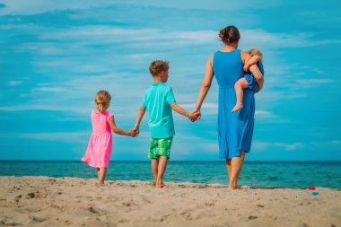 Çocuklu anne tropikal plajda yürüyor.