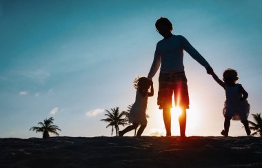 Baba ve küçük kızlar gün batımı kumsalında oynuyorlar, baba ve kızları eğleniyorlar.